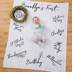 a baby laying on top of a white blanket next to a wreath with writing all over it