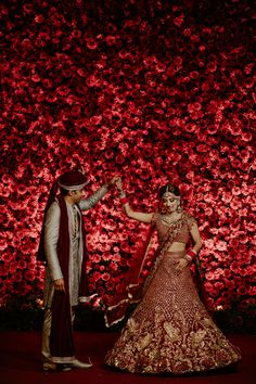 a bride and groom standing in front of a red flower wall at their wedding reception