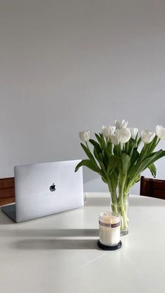 a vase filled with white tulips next to a laptop computer on a table