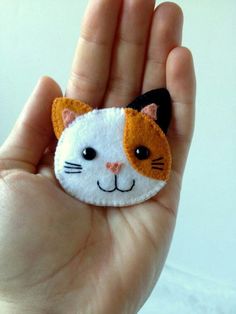 a hand holding a small white and orange cat brooch