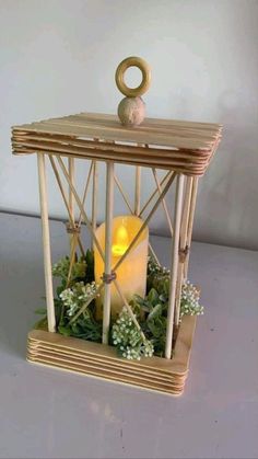 a lit candle in a wooden cage with greenery on the sides and an ornament at the top