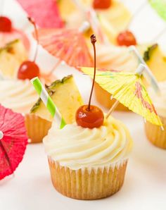 cupcakes decorated with umbrellas and cherries on a white tablecloth, ready to be eaten