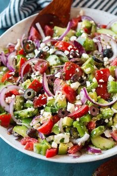 a salad with cucumbers, onions, olives and feta cheese in a white bowl