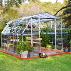 a small greenhouse in the middle of a yard with potted plants and flowers inside