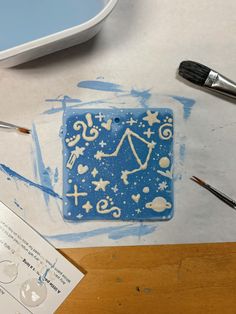 a blue square with white designs on it next to paintbrushes and watercolors