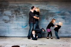 a family kissing in front of a garage door with graffiti on the wall behind them