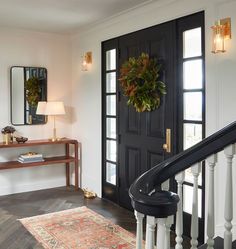 an entryway with a black door, mirror and rug