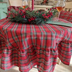 a plaid table cloth with holly and berries on it is sitting in front of two wine glasses