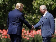 two men in suits shaking hands with each other near some trees and bushes behind them