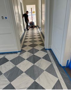 two men are painting the floor in an empty room with white walls and black and white checkered tile