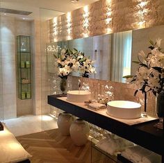 a bathroom with two sinks and flowers in vases next to the mirror on the wall