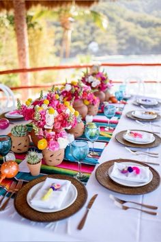 the table is set with colorful flowers and place settings for an outdoor dinner or party