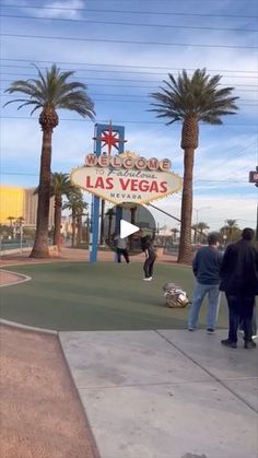 people are standing in front of the las vegas sign and some palm trees on the sidewalk