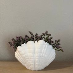 a white shell shaped vase filled with flowers on top of a wooden table next to a wall