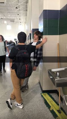 two boys are standing in the hallway with their backpacks on and one boy is leaning against the wall