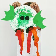 a young boy holding up a paper plate with green and orange decorations on it