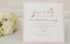 a pink and white wedding card next to some flowers