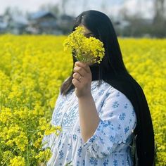 a woman standing in a field holding flowers up to her face and looking at the camera