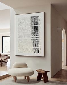 a white chair and ottoman in front of a large art piece on the wall above it