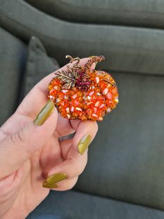 a person holding a small pumpkin shaped brooch in their left hand and green nail polish on the other hand