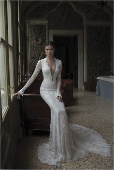 a woman in a white wedding dress standing by a window with her hands on her hips