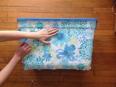 two hands are holding onto a blue and white flowered bag on a wooden floor