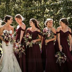 a group of women standing next to each other in front of trees and bushes with bouquets