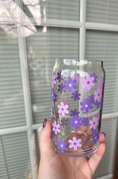 a hand holding a glass with purple flowers painted on the outside and inside, in front of a window