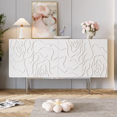 a white sideboard with flowers on it in a living room next to a lamp