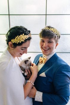 a man in a blue suit holding a cat and smiling at the camera while standing next to a woman wearing a white dress