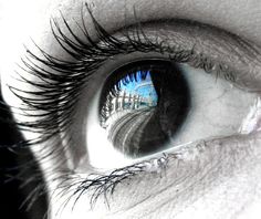 an eye with the reflection of a building in it's blue irise lens