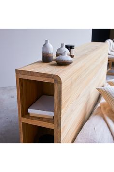 a wooden shelf with two vases on top of it next to a bed and pillows