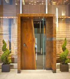 the entrance to an office building with wooden doors and plants in planters on either side