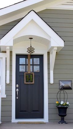 the front door of a gray house with white trim and two black planters on either side