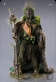 a man dressed up as a creature with plants on his head and arms, holding a stick