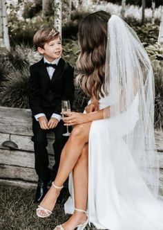 a bride and groom sitting on a bench with champagne in their hands, the boy is wearing a tuxedo