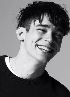 a black and white photo of a young man with his hair in the air smiling