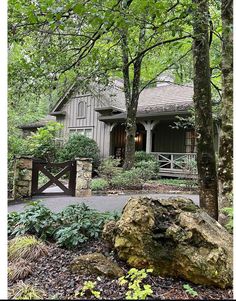 a house in the woods surrounded by trees and rocks, with a large rock on the ground