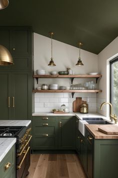 a kitchen with green cabinets and white counter tops, gold pulls on the hoods