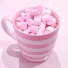 a cup filled with marshmallows on top of a white table next to a pink and white striped mug