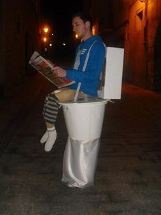 a man sitting on top of a toilet reading a newspaper