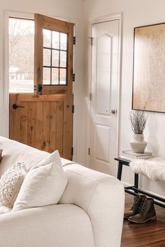 a living room filled with furniture and a wooden door next to a white couch in front of a window