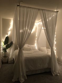 a bed with white curtains and lights on the headboard is in a room that has carpeted flooring