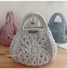 three crocheted purses sitting next to each other on a wooden table in front of a white wall