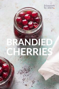 two jars filled with cherries sitting on top of a blue counter next to a white napkin