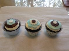 three decorated cupcakes sitting on top of a white table cloth covered in frosting