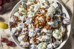 a white bowl filled with fruit and nuts on top of a table next to grapes