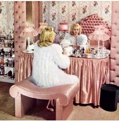 two women sitting at a vanity in a room with pink furniture and wall papered walls