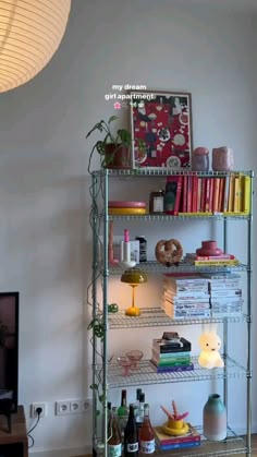 a metal shelf filled with lots of books next to a lamp and a tv on top of a wooden table