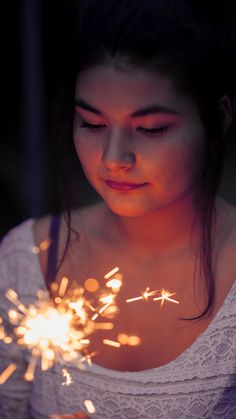 a woman holding a sparkler in her hand and looking down at the ground with eyes closed